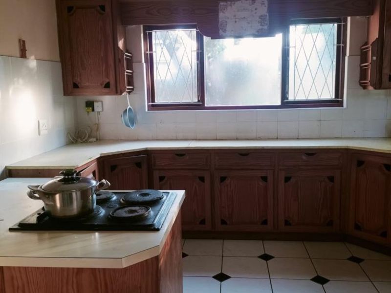 A dated kitchen featuring wooden cabinetry, laminate countertops, an electric hob, and tiled flooring with a classic backsplash.