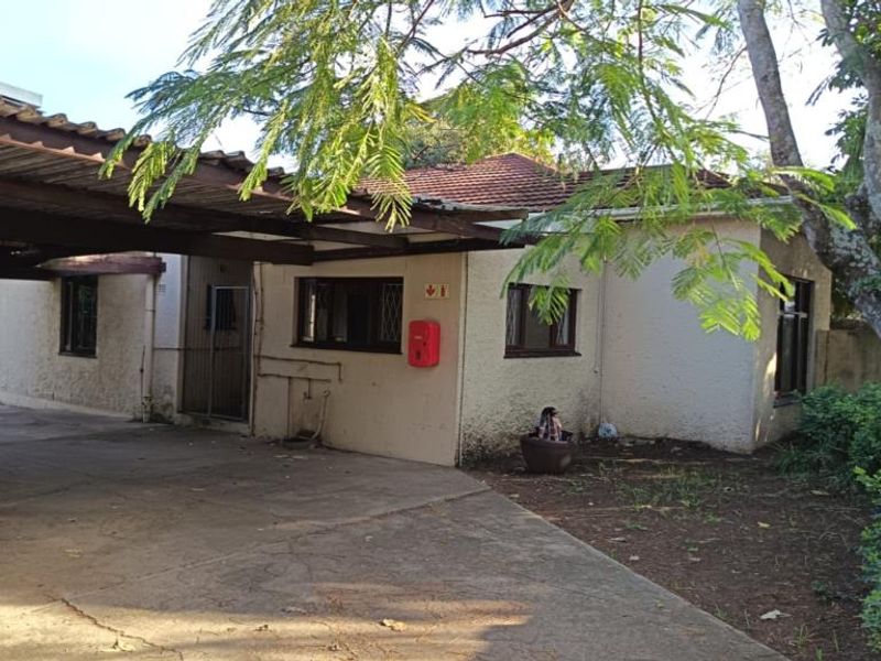 Front exterior view of the property featuring a concrete driveway, attached carport, and security features on windows and doors.