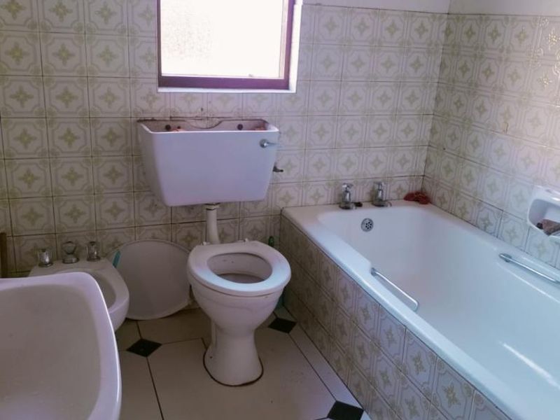 A dated bathroom featuring a bathtub, toilet, bidet, and pedestal sink, requiring modernization and repair of wall tiles and fixtures.