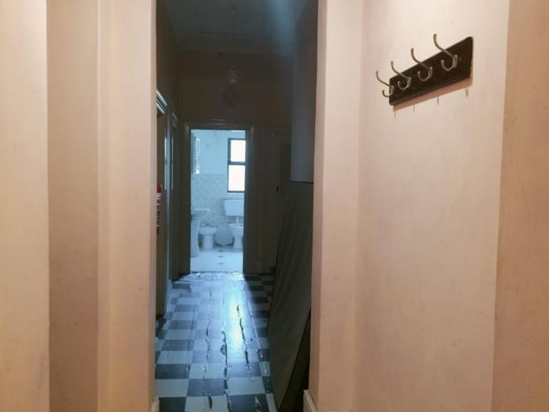 A narrow hallway featuring checkered floor tiles and wall-mounted coat hooks, leading towards a bathroom area.