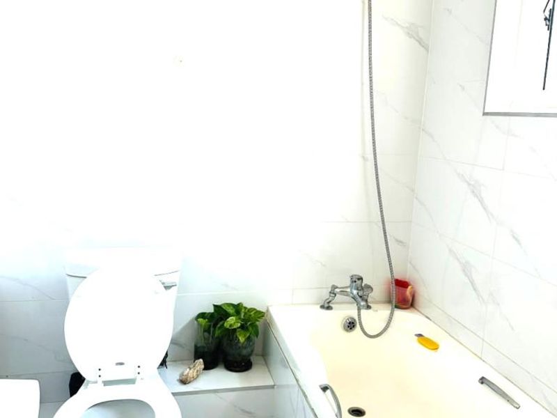 A functional bathroom featuring a bathtub with a handheld shower attachment, a toilet, and marble-look wall tiling.