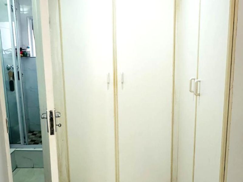 A functional hallway featuring built-in white cupboards and tiled flooring, providing ample storage space with direct access to an adjacent bathroom.