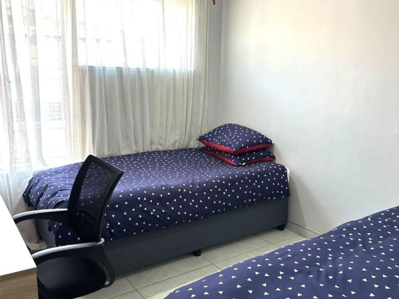 A functional bedroom featuring tiled flooring, a ceiling fan, and large windows with security bars, providing natural light and ventilation.