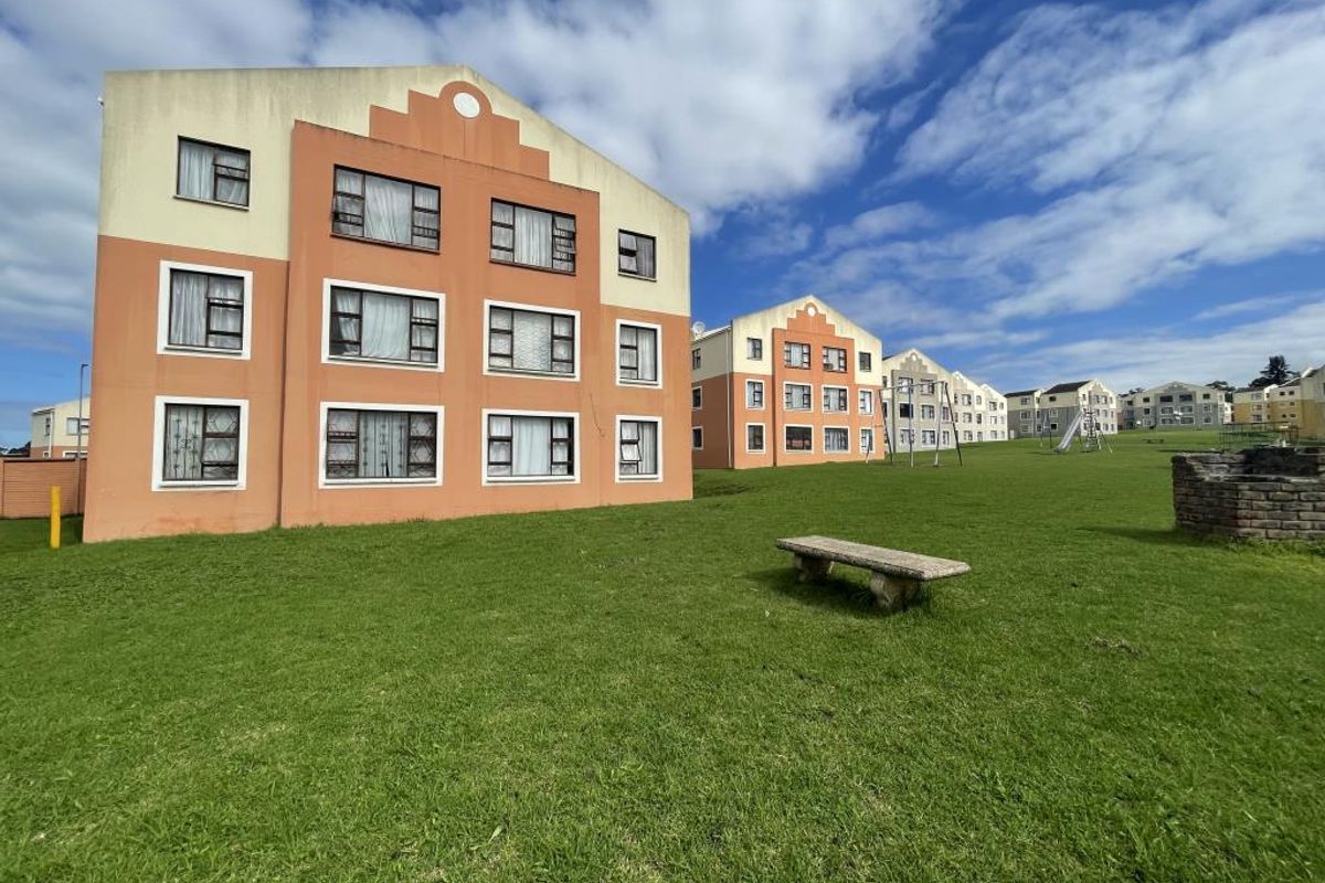 Exterior view of a multi-story apartment complex featuring landscaped communal green spaces and paved pathways.