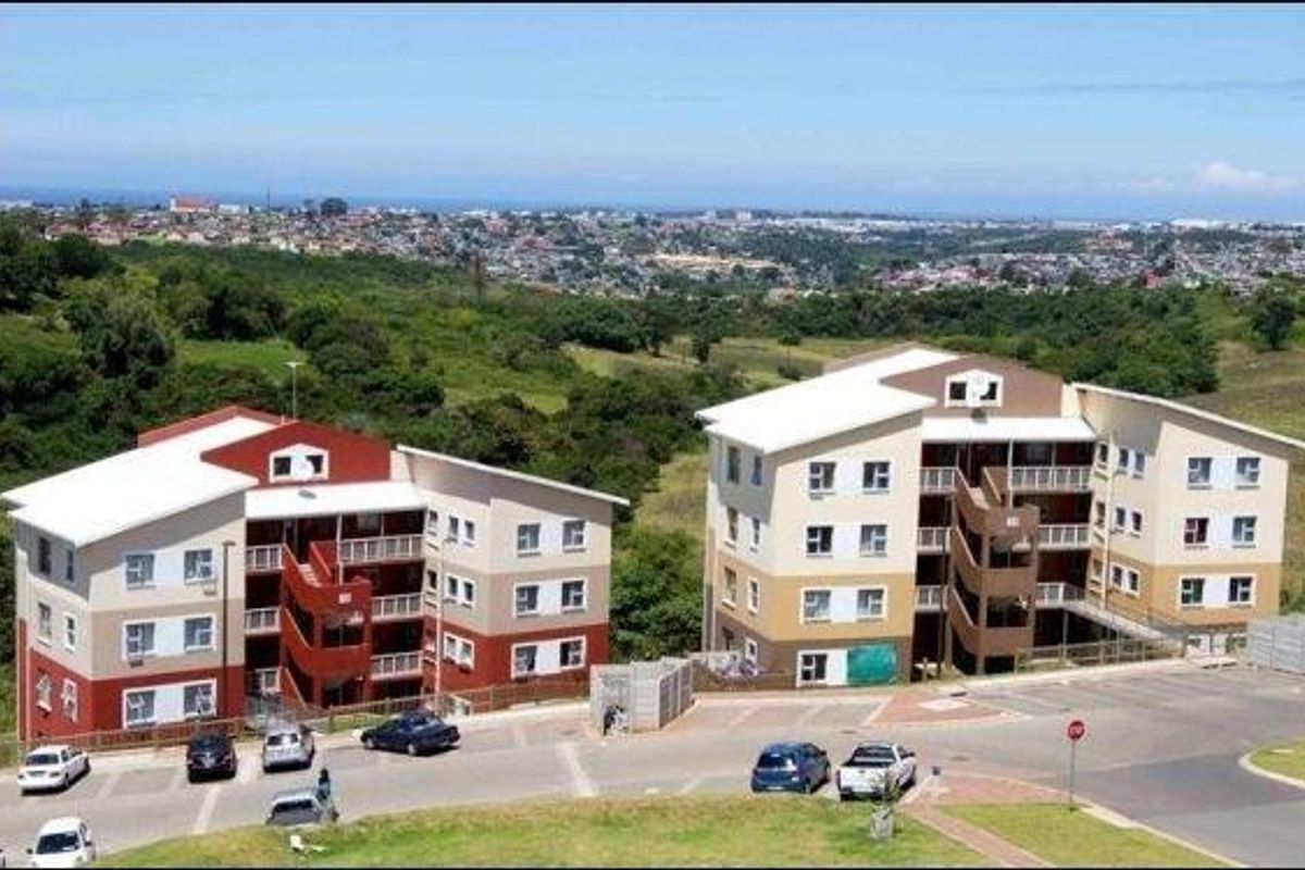 Aerial view of two multi-story apartment buildings featuring pitched roofs, external staircases, and an adjacent paved parking area set against a landscape background.