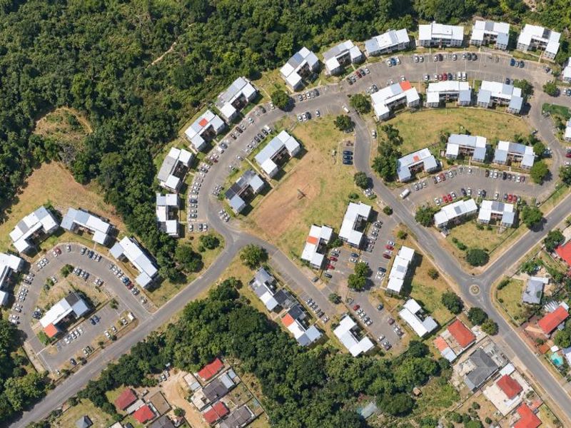 An aerial view of a residential apartment complex featuring multiple building blocks, paved parking areas, and surrounding green space.