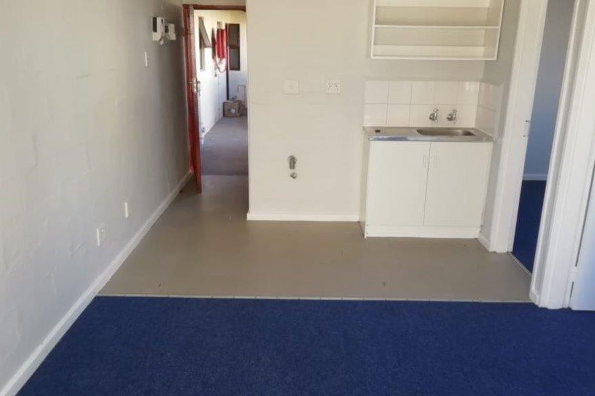 A compact, empty kitchen area featuring basic built-in cabinetry, a stainless steel sink, and tiled splashback, offering potential for modernization.