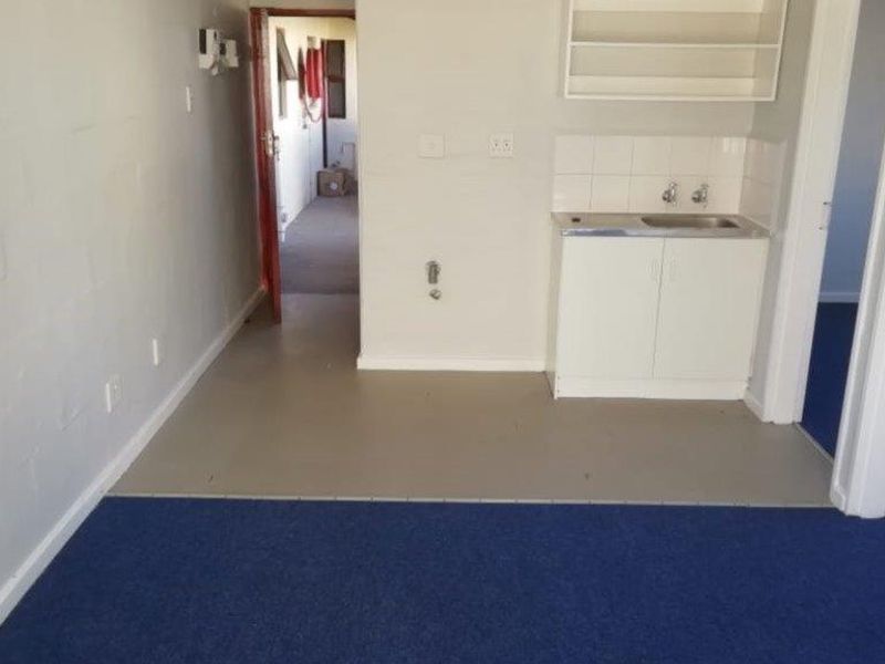 A compact, empty kitchen area featuring basic built-in cabinetry, a stainless steel sink, and tiled splashback, offering potential for modernization.