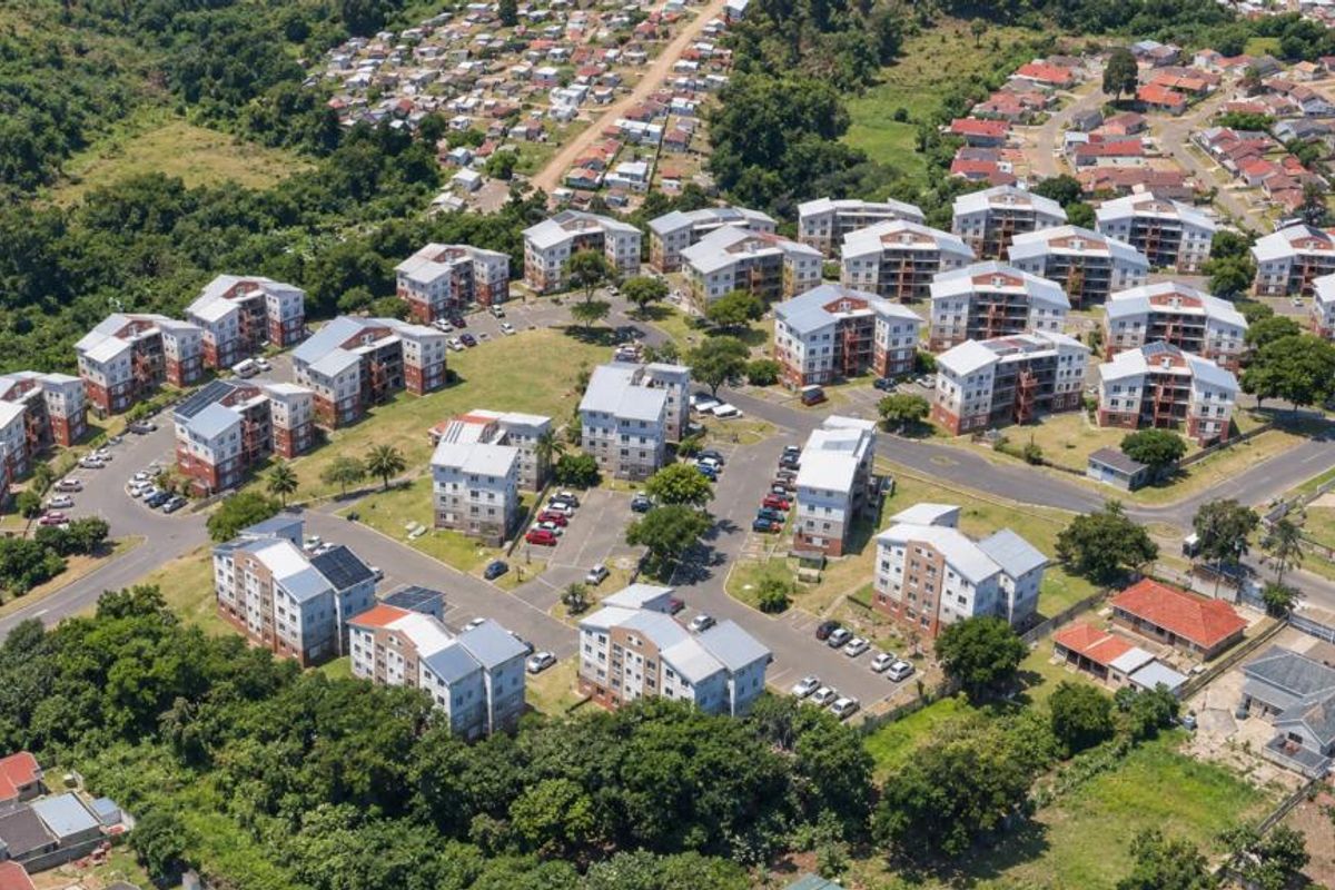 An aerial view of a residential apartment complex featuring multiple multi-story buildings, paved parking, and surrounding green spaces within a suburban neighborhood.