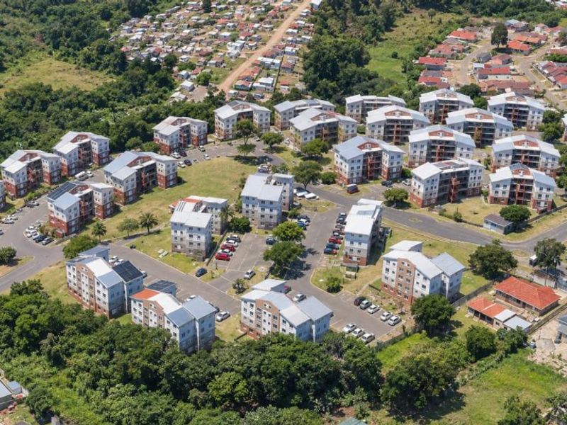 An aerial view of a residential apartment complex featuring multiple multi-story buildings, paved parking, and surrounding green spaces within a suburban neighborhood.
