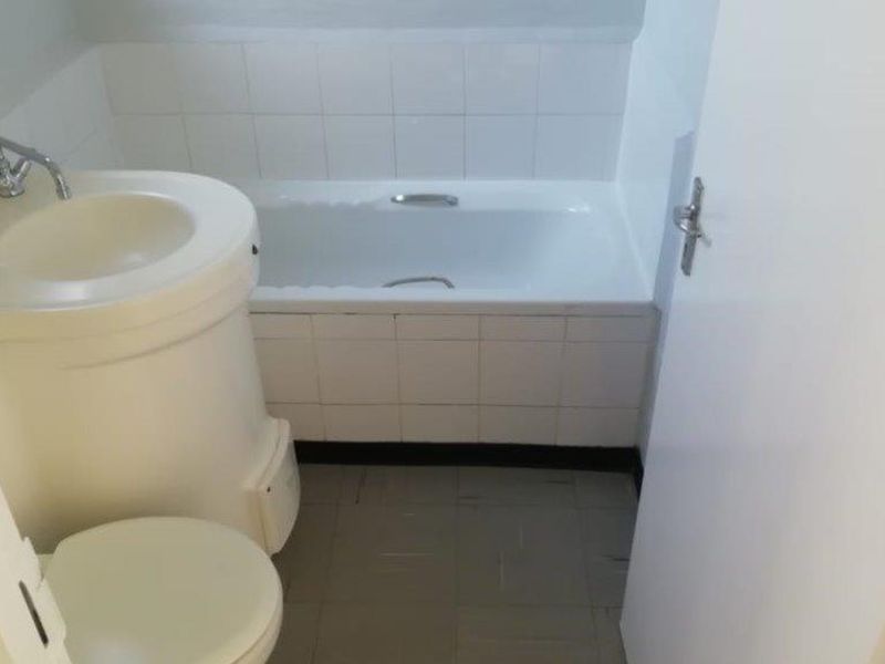 A compact, dated bathroom featuring a white bathtub, pedestal basin, and toilet with tiled splashbacks and flooring.