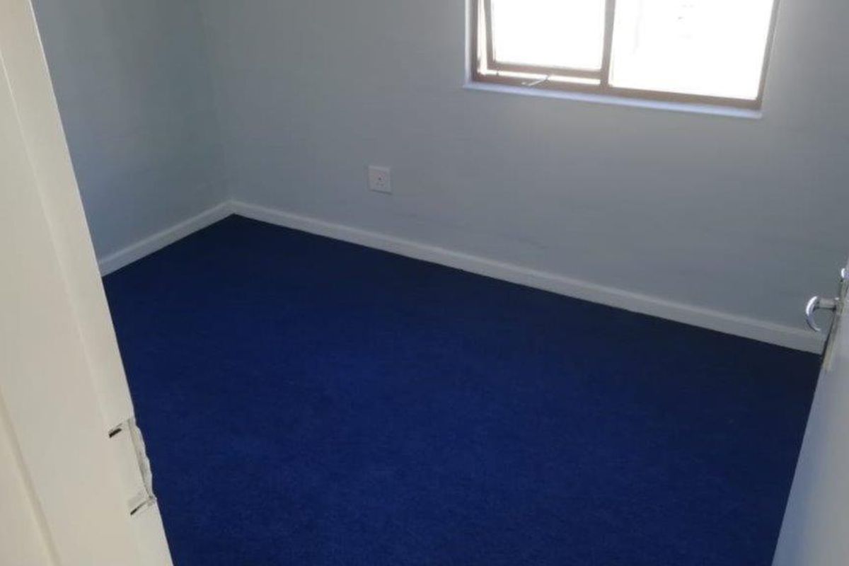 A clean, empty bedroom featuring blue carpeting and a sliding window, providing a neutral blank canvas for personalization.