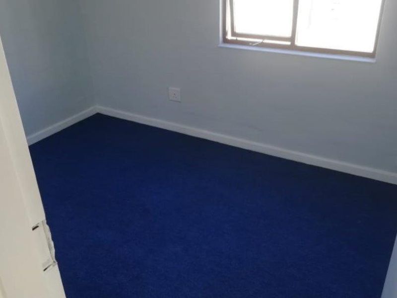 A clean, empty bedroom featuring blue carpeting and a sliding window, providing a neutral blank canvas for personalization.