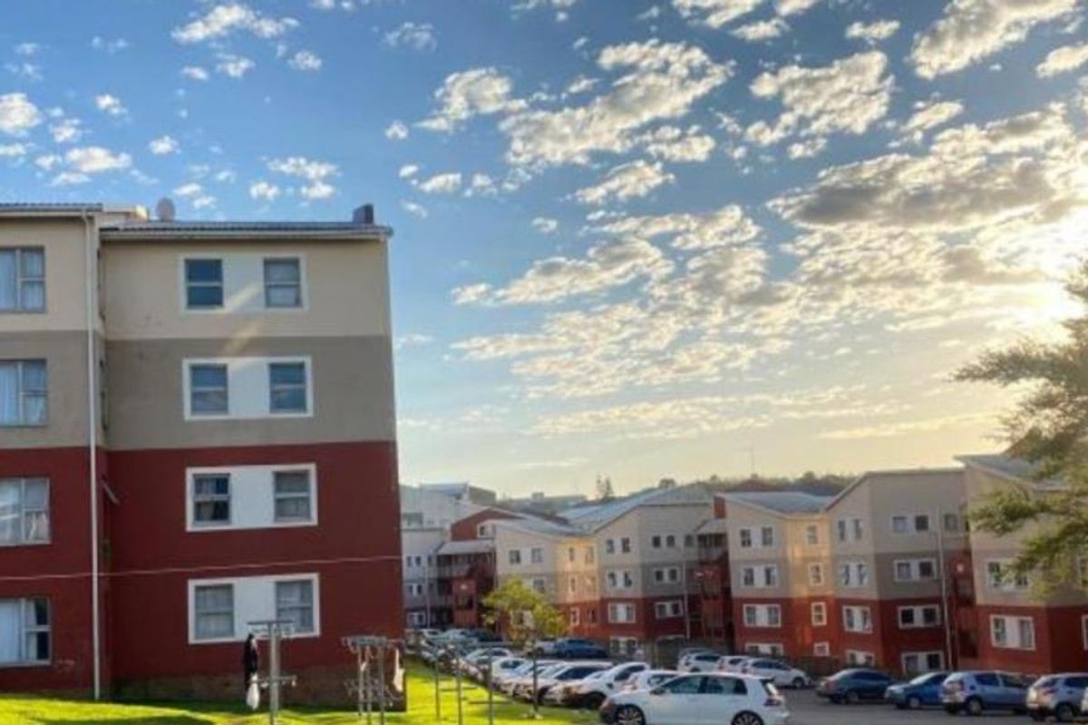 Exterior view of multi-story apartment blocks featuring a paved parking area and landscaped grounds under a clear sky.