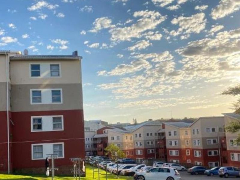 Exterior view of multi-story apartment blocks featuring a paved parking area and landscaped grounds under a clear sky.