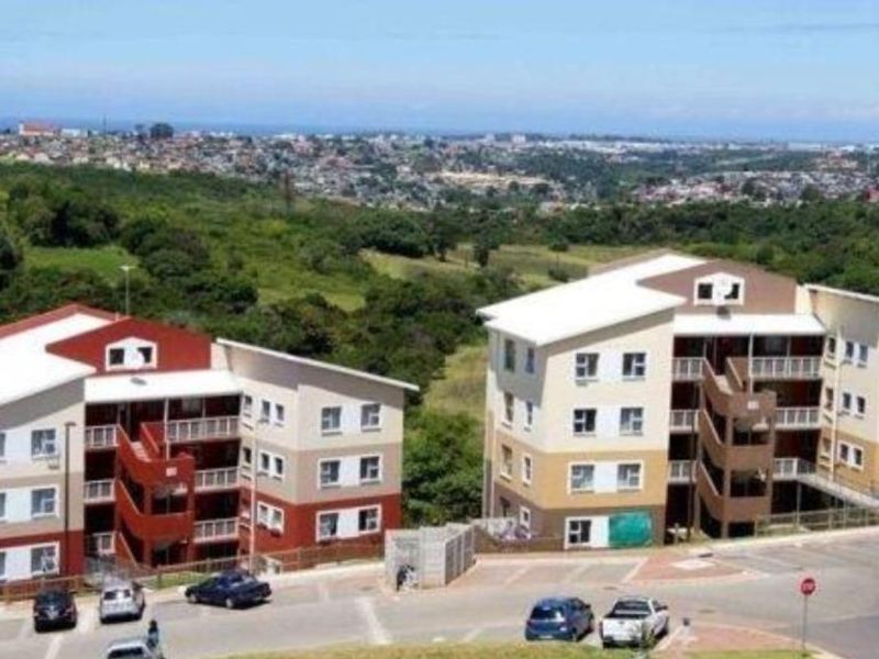 An aerial view of two multi-story apartment buildings featuring external staircases, balconies, and an adjacent paved parking area set against a suburban landscape.