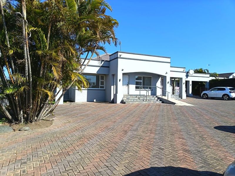 Front view of a commercial property featuring a paved driveway, stone entrance steps with metal handrails, and a well-maintained exterior facade.