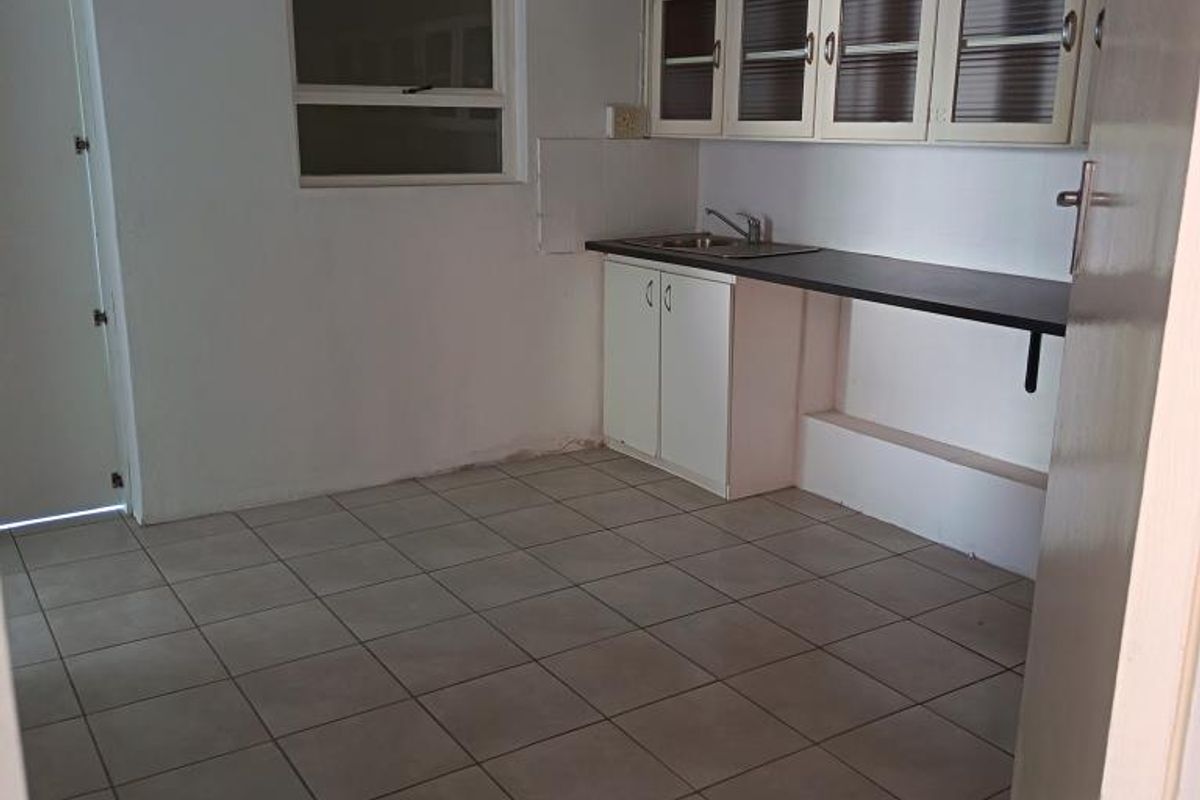 A compact, empty kitchen area featuring tiled flooring, built-in cabinetry, a laminate countertop with a sink, and an overhead extractor fan.