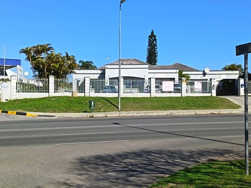 Front exterior view of a commercial property featuring a secure perimeter fence, concrete pillars, and a tiled roof, situated along a main road.