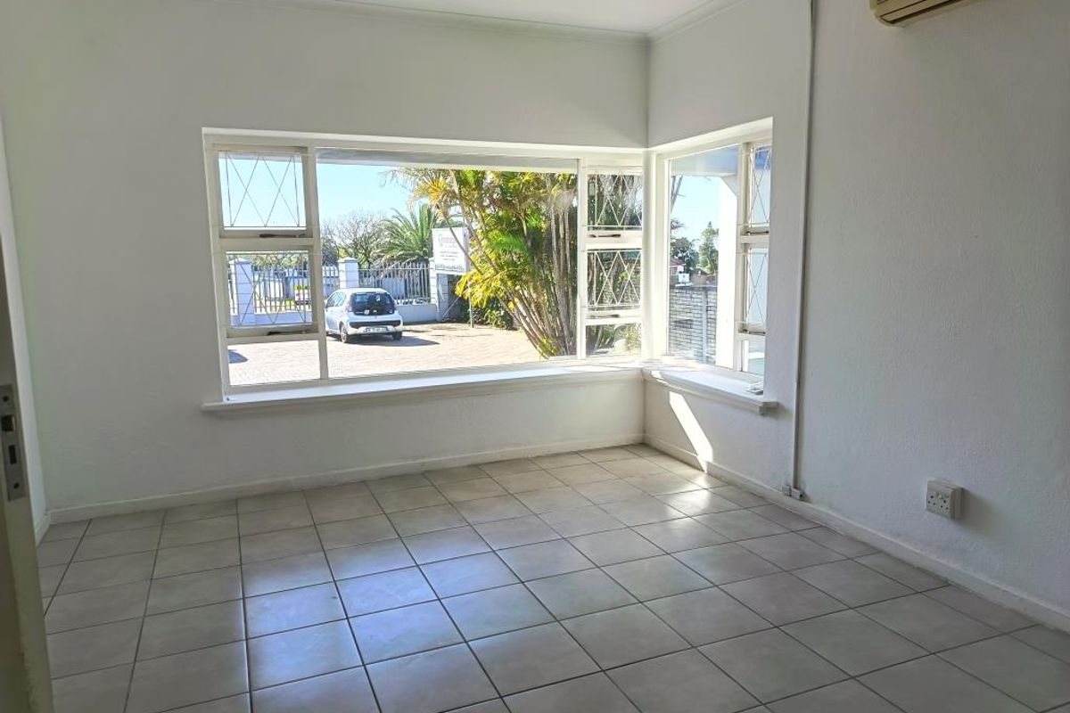 A bright, empty commercial office or living space featuring large corner windows, tiled flooring, and a wall-mounted air conditioning unit.