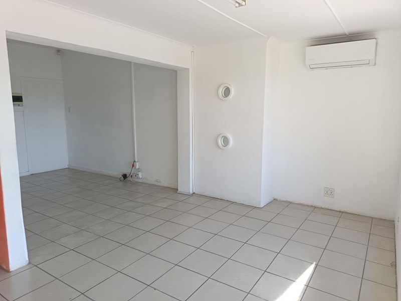 An empty, open-plan commercial space featuring neutral tiled flooring, a wall-mounted air conditioning unit, and unique circular wall accents.