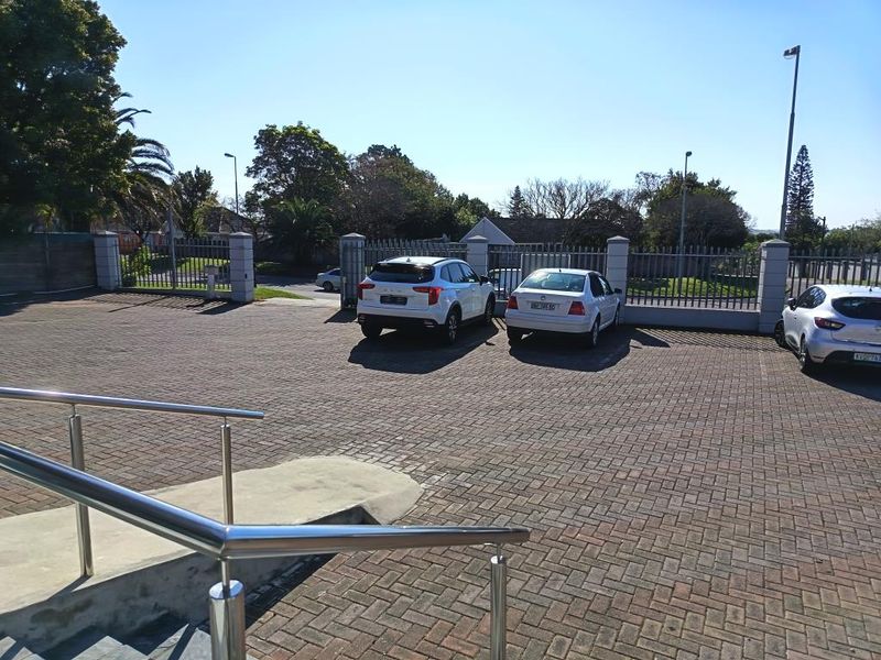 Commercial property exterior featuring a paved parking area, secure steel perimeter fencing, and a concrete access ramp with stainless steel handrails.