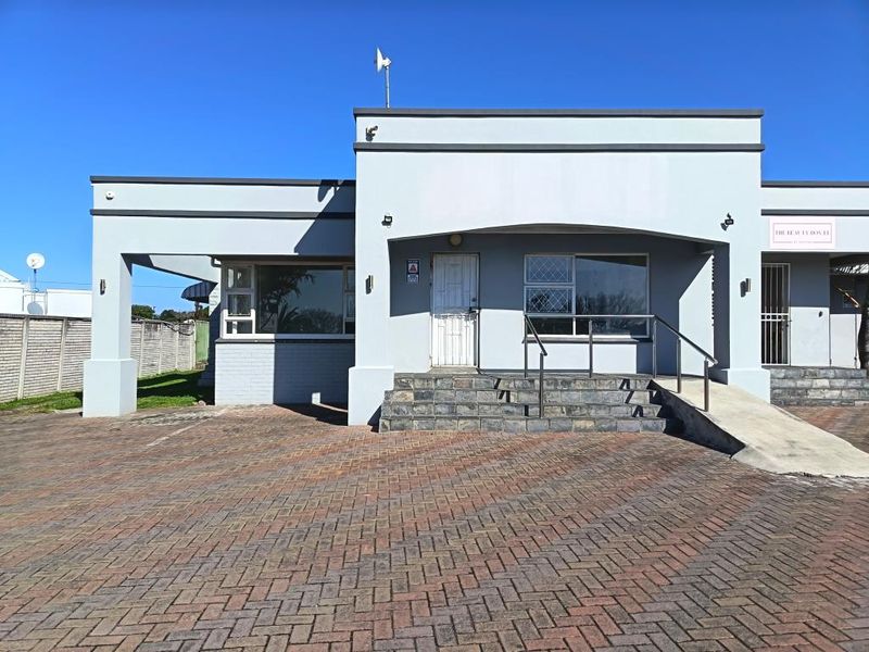 Front elevation of a commercial property featuring a paved driveway, stone-clad entrance steps, and a wheelchair-accessible ramp with security features.