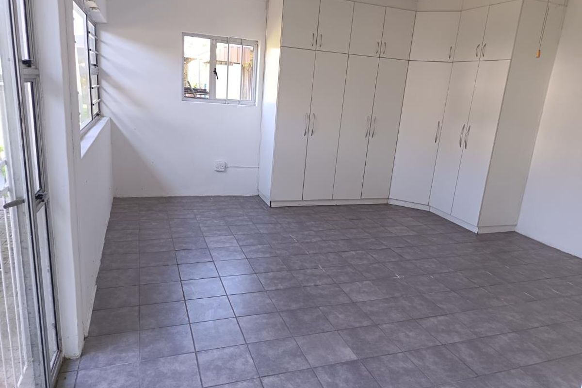 A bright, empty bedroom featuring neutral tiled flooring and extensive white built-in cupboards, offering ample storage space and a clean, functional layout.