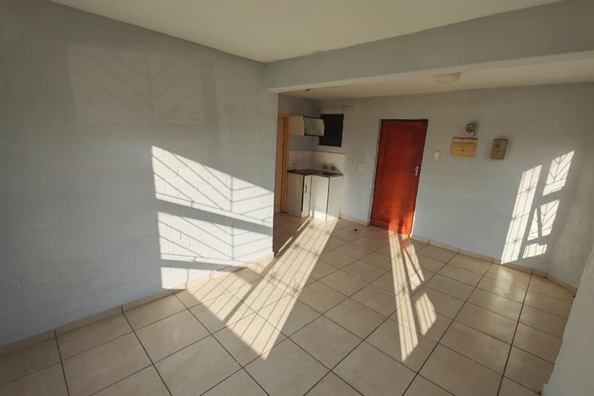 An open-plan living area featuring tiled flooring and a compact kitchenette, offering a blank canvas for potential renovation and interior design.