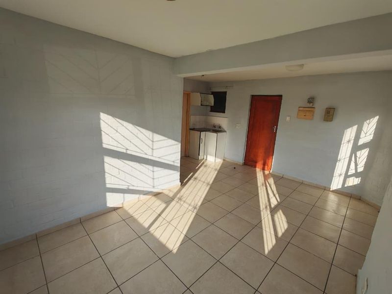 An open-plan living area featuring tiled flooring and a compact kitchenette, offering a blank canvas for potential renovation and interior design.