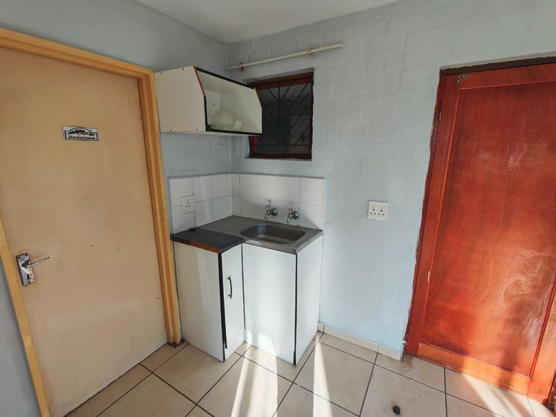 A functional laundry area featuring a stainless steel sink, tiled splashback, and built-in cabinetry, finished with ceramic floor tiles.