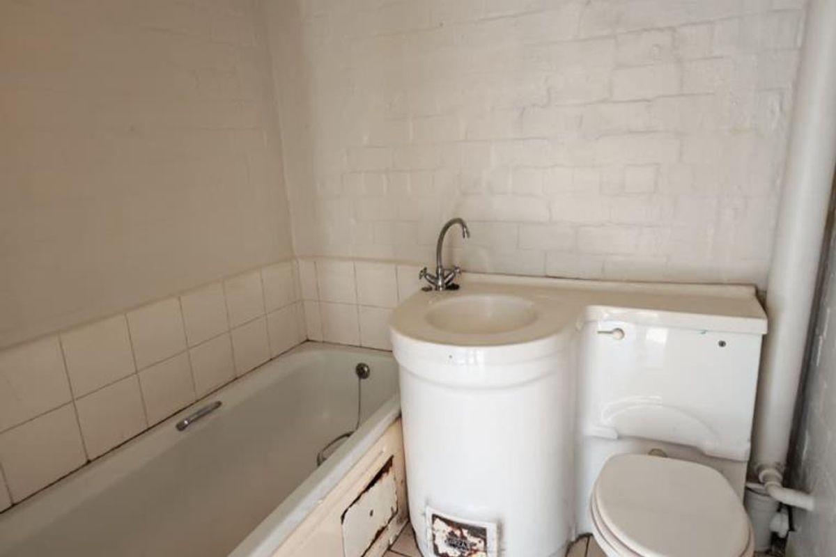 A dated bathroom featuring a combined basin and toilet unit, a standard bathtub, and tiled finishes, requiring modernization and repair of fixed fixtures.