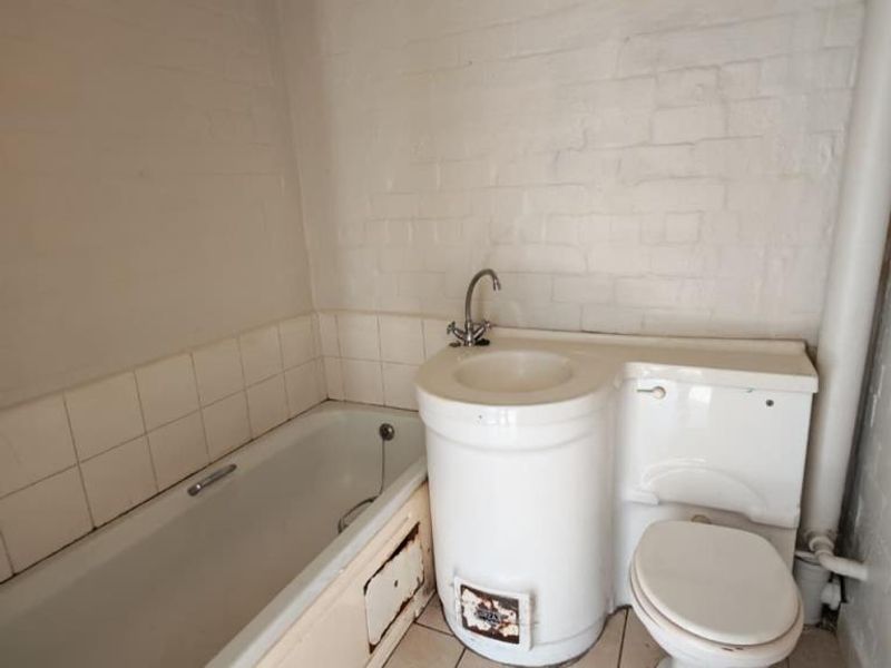 A dated bathroom featuring a combined basin and toilet unit, a standard bathtub, and tiled finishes, requiring modernization and repair of fixed fixtures.