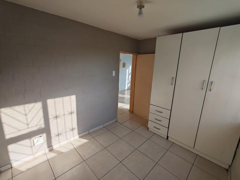 A clean, empty bedroom featuring neutral grey walls, tiled flooring, and a functional built-in wardrobe with integrated drawers.