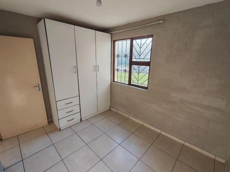 A compact bedroom featuring tiled flooring, a built-in wardrobe, and a window fitted with security bars.