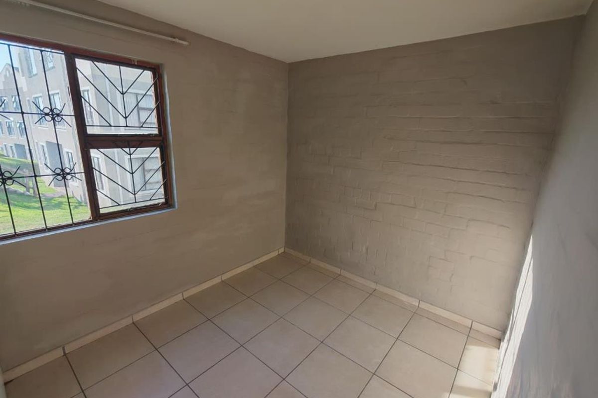 An empty bedroom featuring tiled flooring, security bars on the window, and unfinished exposed brick walls, offering a blank canvas for renovation.