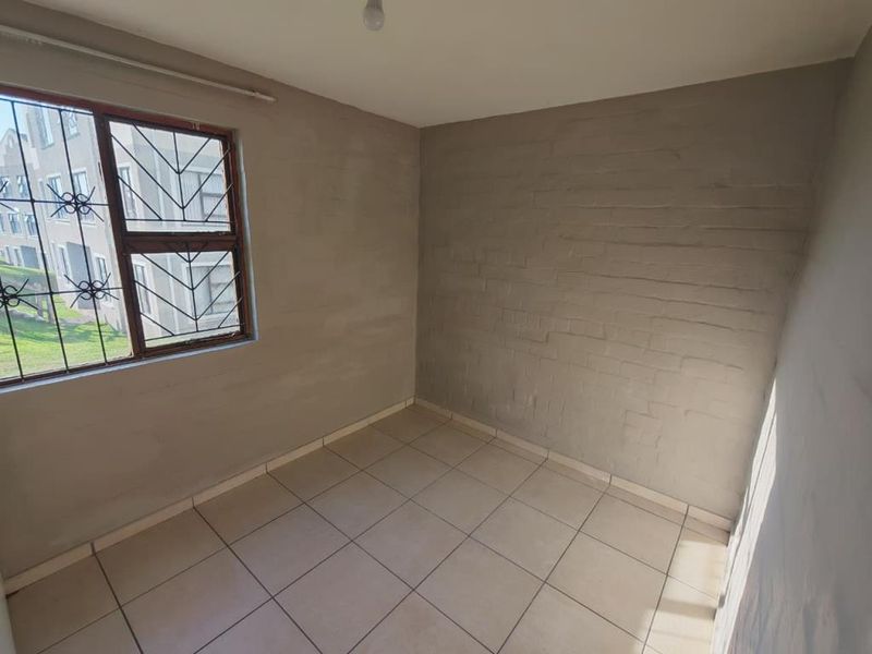 An empty bedroom featuring tiled flooring, security bars on the window, and unfinished exposed brick walls, offering a blank canvas for renovation.