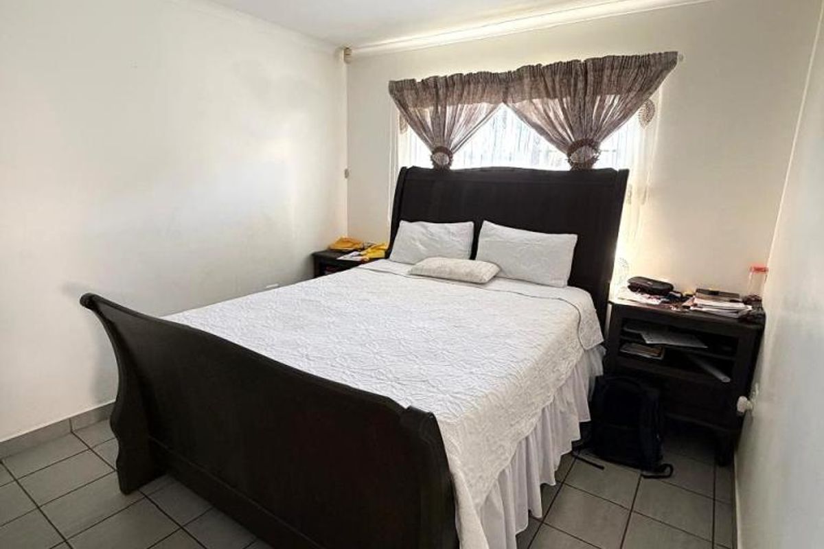A bedroom featuring tiled flooring and a window with fitted curtain rails.