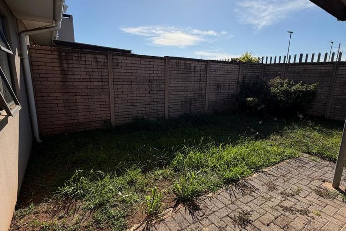 A private rear garden area featuring a paved patio section and a lawn area enclosed by a brick boundary wall.