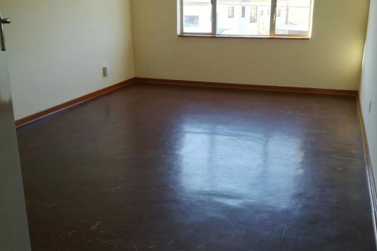 A spacious, empty bedroom featuring large windows, dark vinyl flooring, and neutral wall paint, offering a blank canvas for personalization.