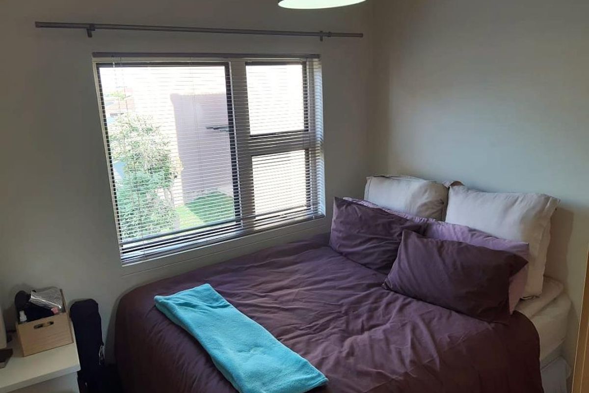 A functional bedroom featuring a window with fitted horizontal blinds and a central ceiling light fixture.