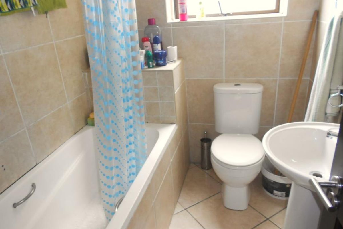 A compact bathroom featuring a bathtub with shower attachment, a pedestal basin, and a standard toilet, finished with neutral wall and floor tiling.