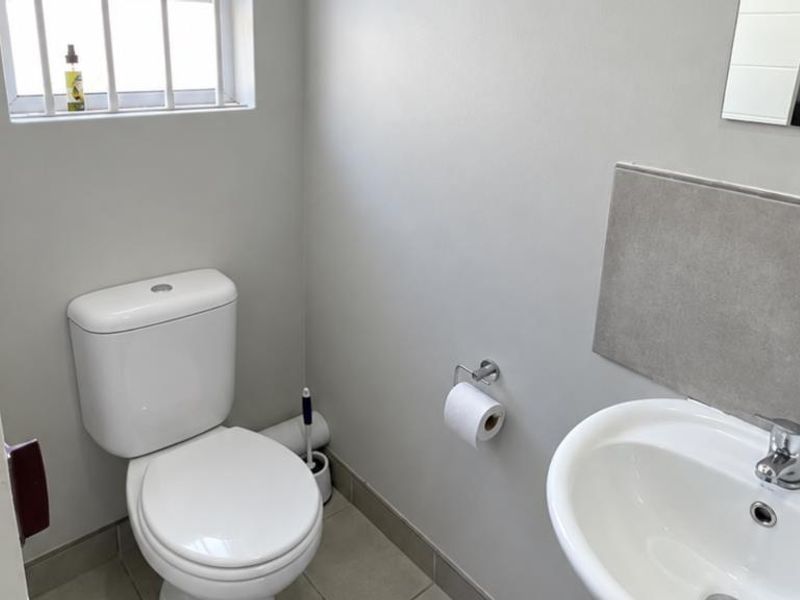 A clean and functional guest bathroom featuring a white toilet, pedestal basin with chrome mixer tap, and neutral tiled finishes.