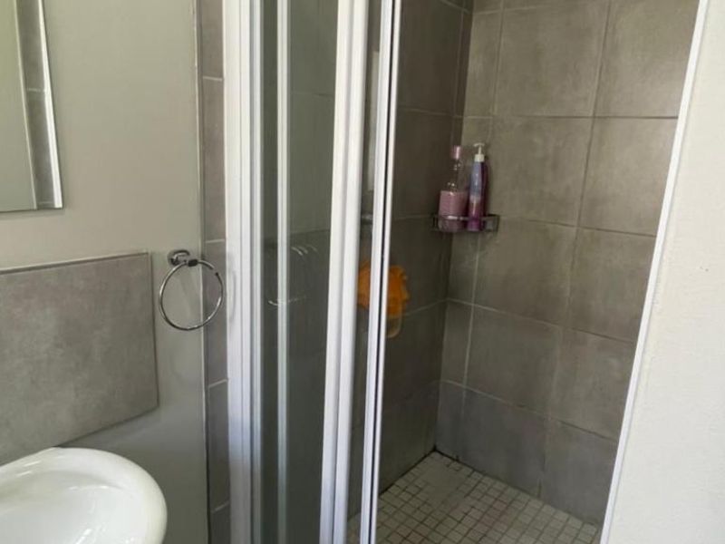 A functional bathroom featuring a tiled shower enclosure with a glass door, a pedestal basin, and a wall-mounted mirror.
