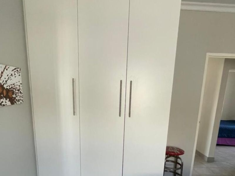 A bedroom featuring a clean, white built-in wardrobe with modern handles and decorative coving along the ceiling.