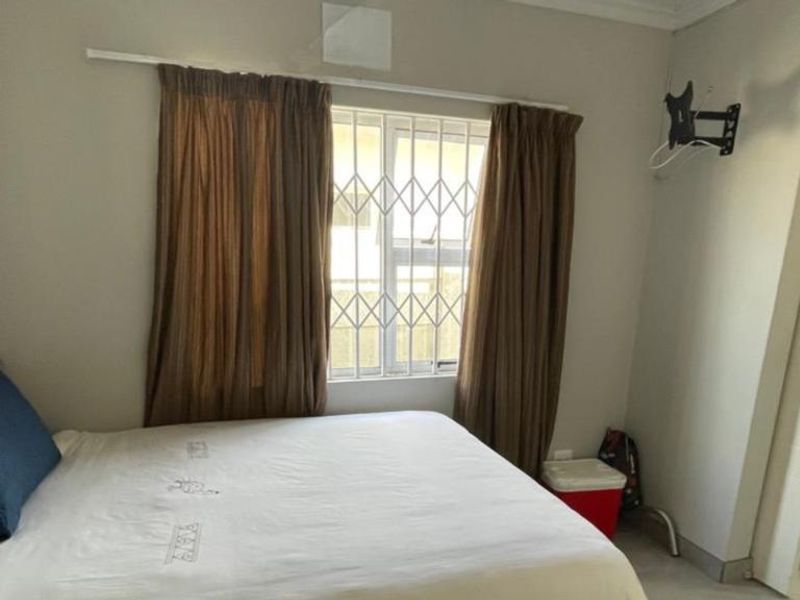 A functional bedroom featuring tiled flooring, security bars on the window, and a wall-mounted television bracket.