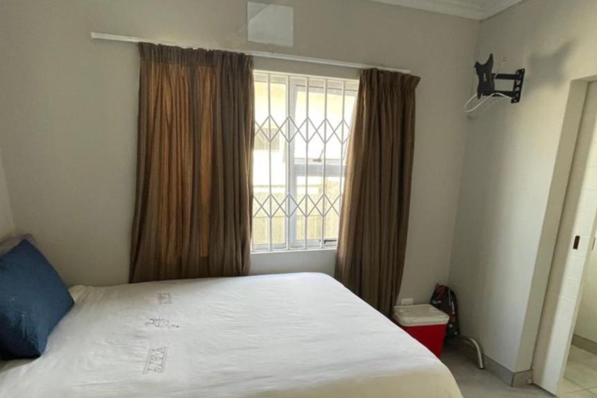 A functional bedroom featuring tiled flooring, security bars on the window, and a wall-mounted television bracket.