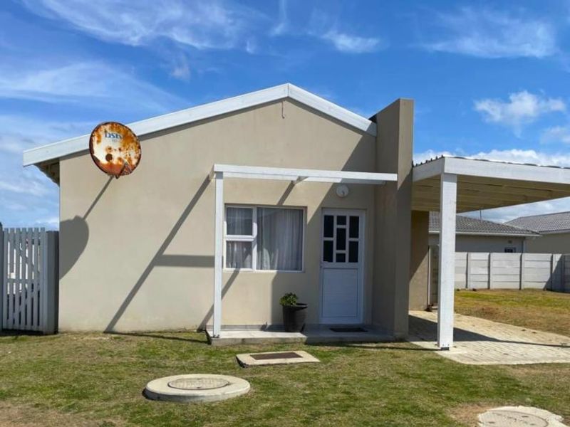 Front view of a single-story house featuring a covered patio, paved driveway, and precast concrete boundary walling.
