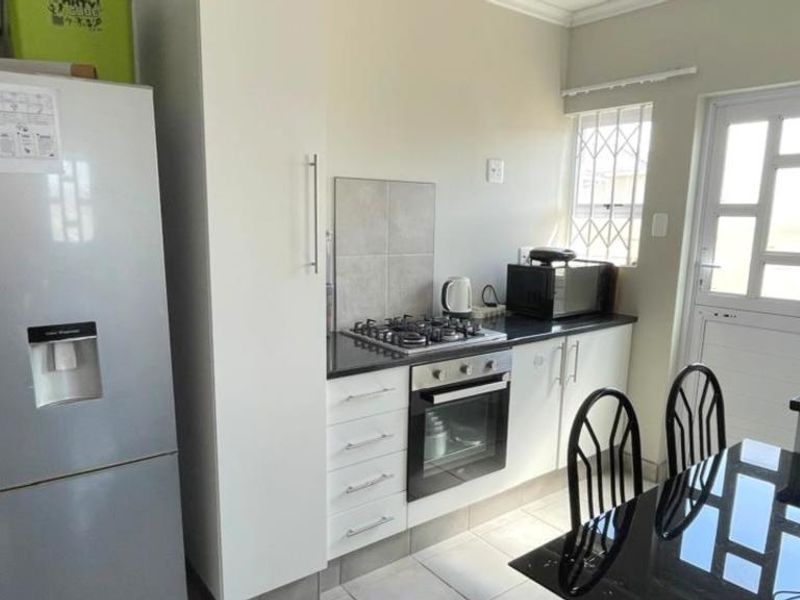 A functional kitchen featuring a gas hob, built-in oven, tiled flooring, and direct access to the exterior via a security door.