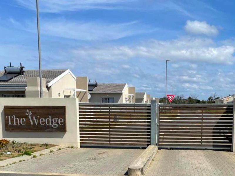 The gated entrance to The Wedge residential estate, featuring a paved driveway, perimeter walling, and modern housing units with solar water heaters.